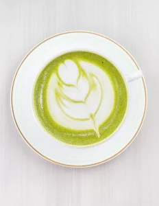 A vibrant green matcha latte, shown both hot in a cup and cold in a glass with ice.