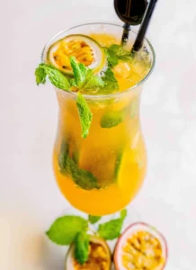 A bright orange or yellow mocktail with passion fruit and a garnish.