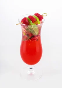 A glass of raspberry mojito with fresh raspberries, mint, and lime wedges.