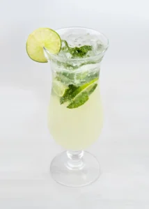 A glass of virgin mojito with mint leaves and lime wedges.
